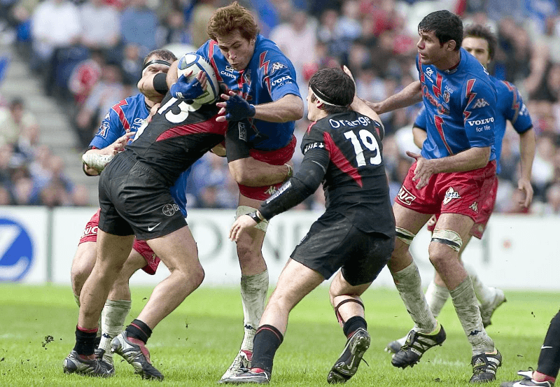 An image of rugby players on the field involved in a tackle