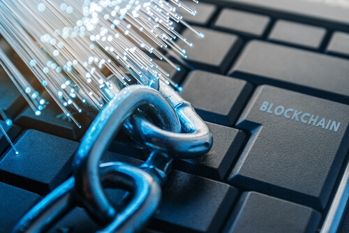 Links of a chain and a bundle of optic fibres lay on a keyboard with the word 'blockchain' on the enter key