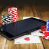 A smartphone on top of playing cards surrounded with poker chips