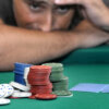 A man with an upset expression looks at poker chips and playing cards across a green felt table